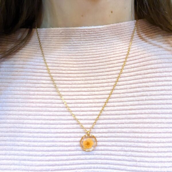 a girl in a pink shirt wearing a dainty necklace with a circle frame pendant with a little orange real pressed flower inside