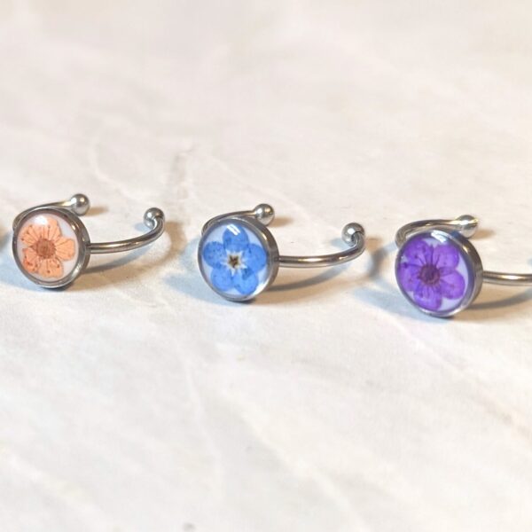 3 rings with circle tops and real flowers inside - a orange flower, blue flower, and purple flower