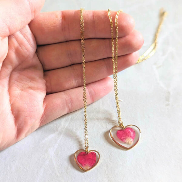 a hand holding two necklaces heart shaped with real rose petals inside