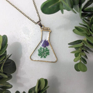 a little broze beaker framed necklace with 2 real flowers inside like a potion