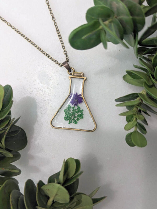 a little broze beaker framed necklace with 2 real flowers inside like a potion