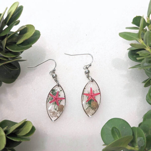 almond-shaped dangle earrings with a transparent background and inside is a real starfish, seaweed, a snail shell, and sand